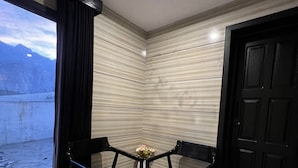 Habitación de esquina con puerta negra, ventana con vista a montañas y una mesa con dos sillas.