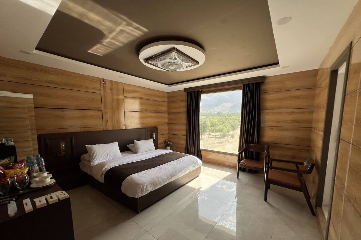 Camera da letto moderna con un letto grande, pareti in pannelli di legno, una ventola a soffitto e vista su un paesaggio montuoso.
