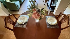 Una mesa redonda de madera con dos sillas, cada una con un mantel individual estampado. Un jarrón con flores está colocado en el centro de la mesa.