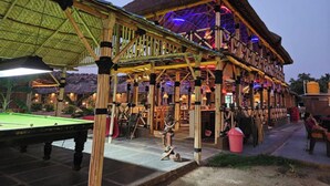 Une structure en bois avec un toit de chaume, une table de billard et un espace bar de style tiki.