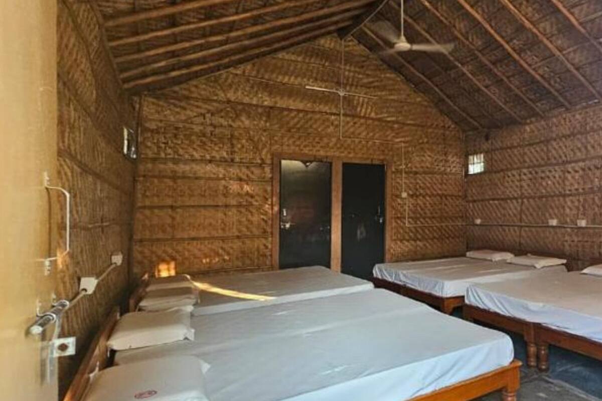 Une pièce rustique avec quatre lits en bois alignés contre le mur, une porte et un ventilateur de plafond.