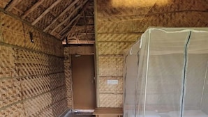 Une pièce avec un plafond en pente, des murs en bois, un lit doté d’une moustiquaire et un petit banc en bois.