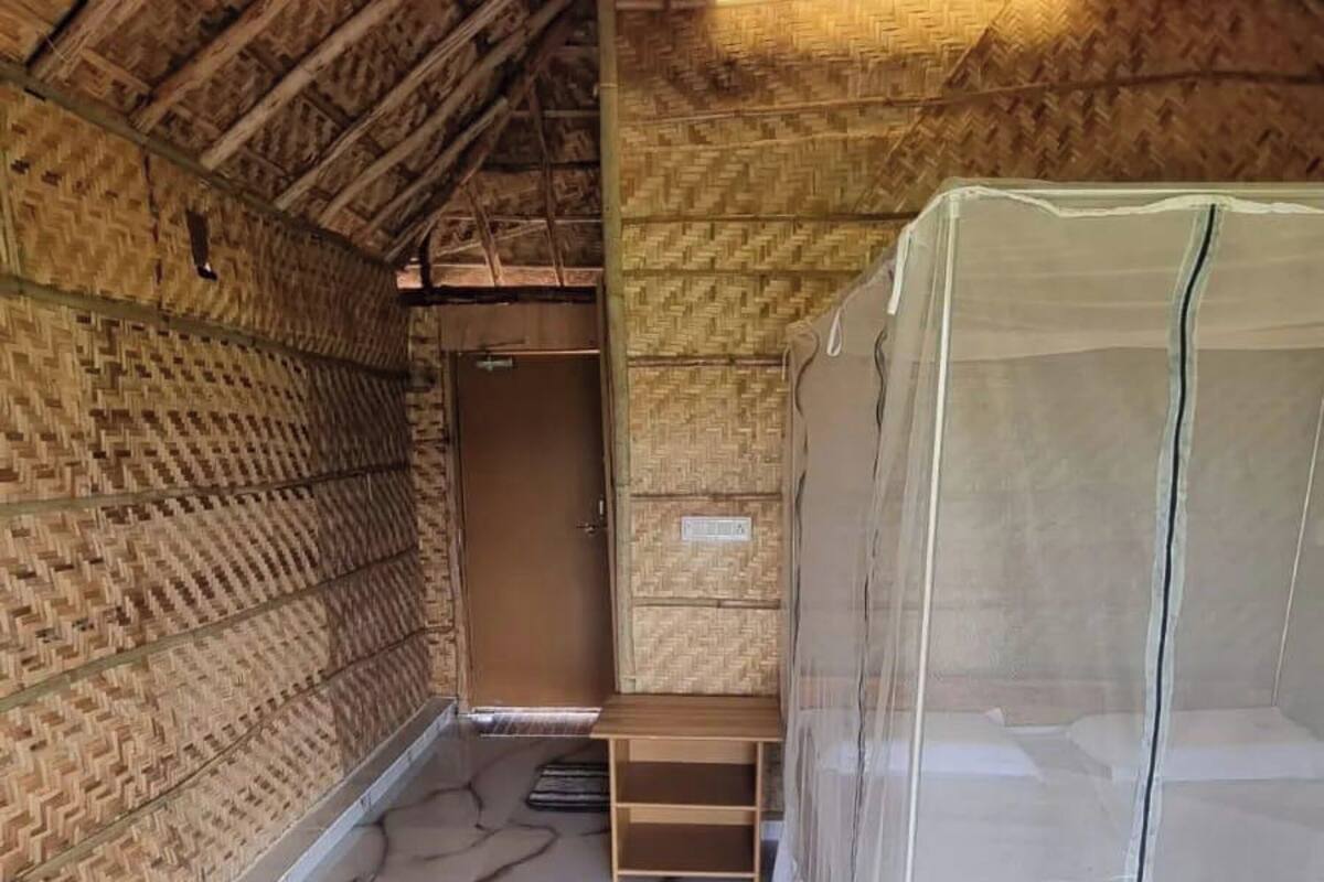 Une pièce avec un plafond en pente, des murs en bois, un lit doté d’une moustiquaire et un petit banc en bois.