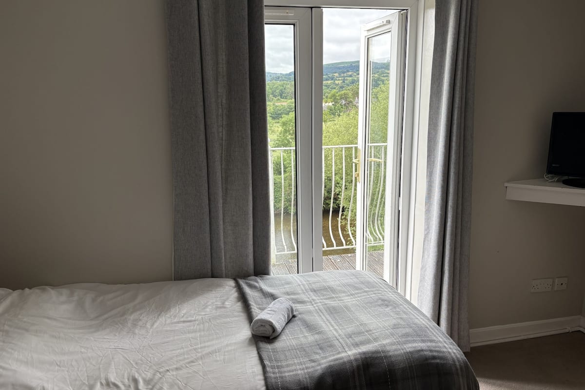 Una camera da letto con un letto, una TV su uno scaffale e un balcone con vista sul verde.