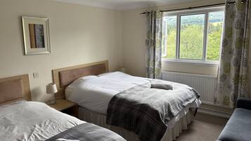 A bedroom with two beds, a window with curtains, a bedside table with a lamp, and a framed picture on the wall.