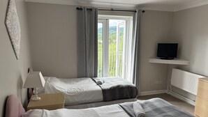 A bedroom with two beds, a television on a shelf, and a window with curtains.
