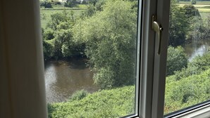 A window with a view of a river and greenery, a door handle, and a window frame.