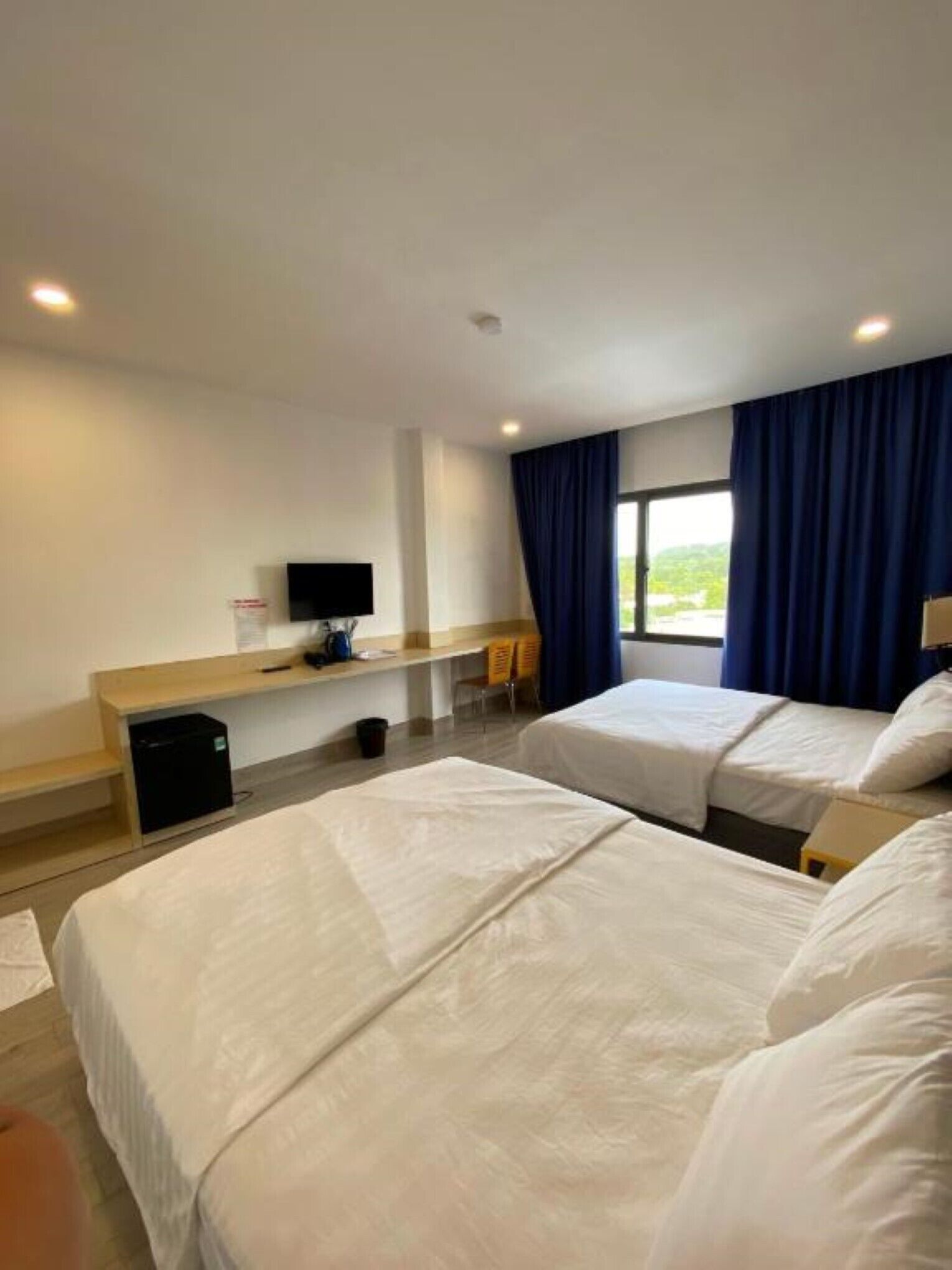 A hotel room with two beds, a desk with a computer, and a window with curtains.