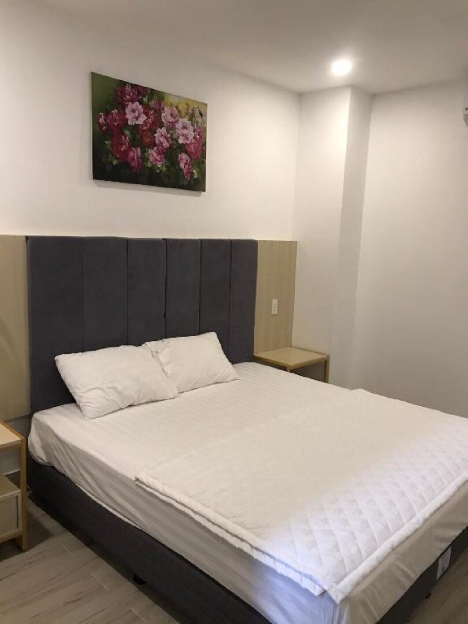 A bedroom with a bed, a nightstand, a wall-mounted painting, and a bedside table.
