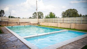 Ein rechteckiger Pool mit Steinrand, umgeben von einer niedrigen Steinmauer und einer Rasenfläche.