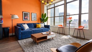 A modern living room with a blue sofa, a coffee table, and a city view through large windows. - McCormick South Loop 2BR Suite Near Soldier Field & Museum Campus (Chicago)