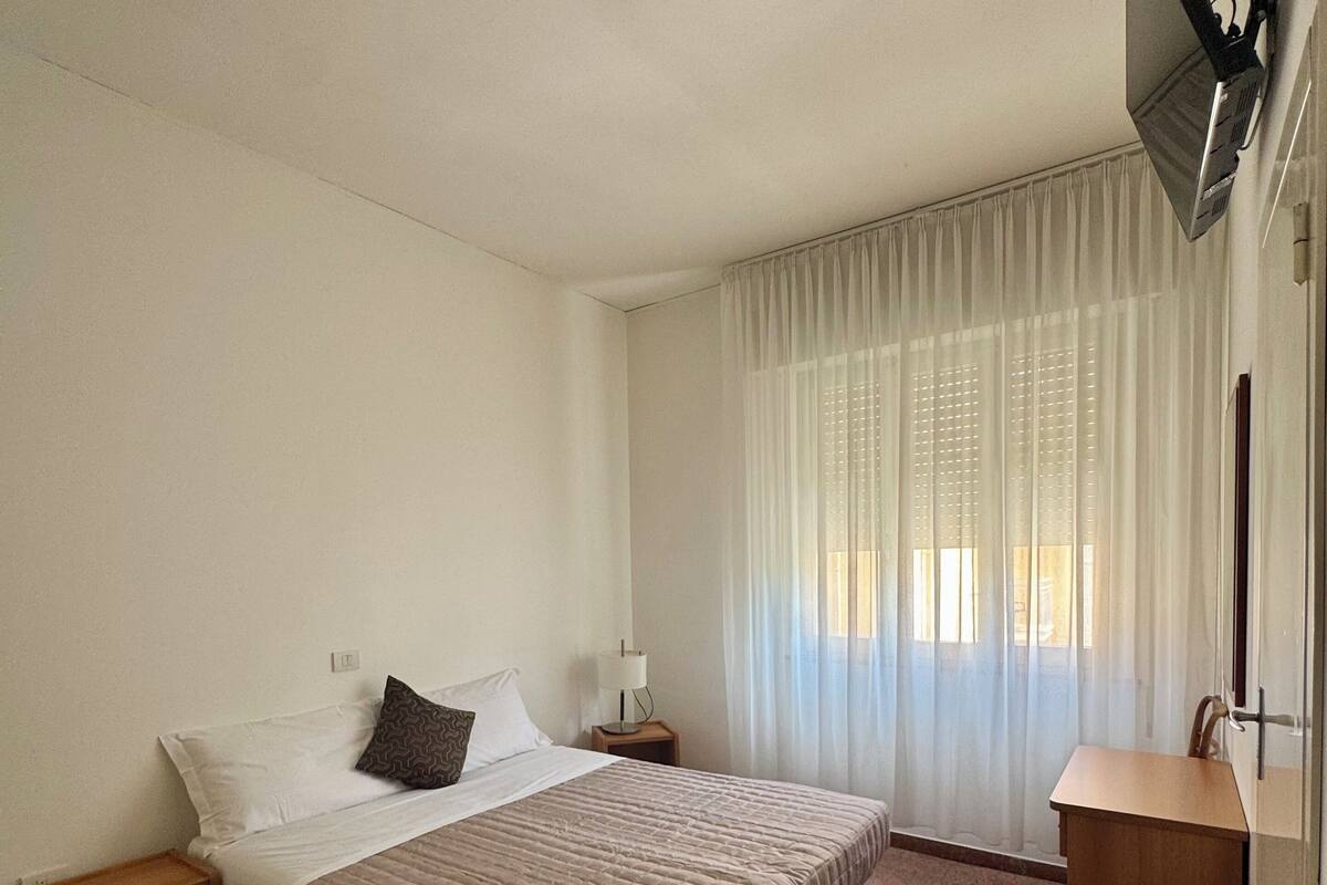 Habitación de hotel con cama, mesita de noche, espejo y ventana con cortinas.