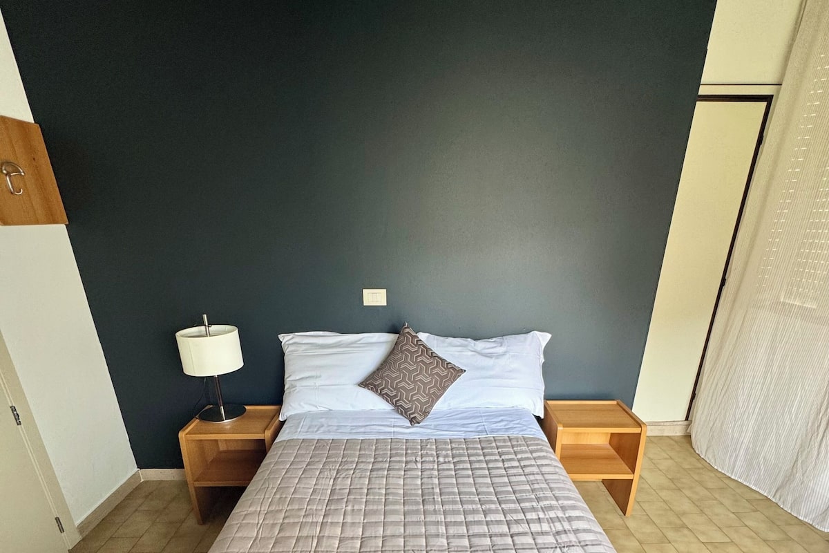 Una cama con cubrecama acolchado, dos mesitas de noche con lámparas y una pared oscura.