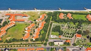 An aerial view of a coastal residential area with rows of houses, a beach, and a large building with a red roof. - 6 Person Holiday Park Home in Saeby (Sæby)