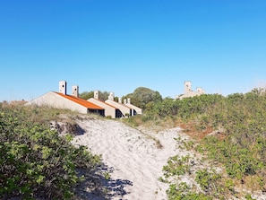 Ein Küstengebäude mit mehreren Schornsteinen, ein Sandweg davor und umliegende Vegetation.