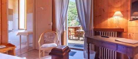 Um quarto de madeira com uma cama, uma cadeira, uma mesa e uma janela com cortinas.