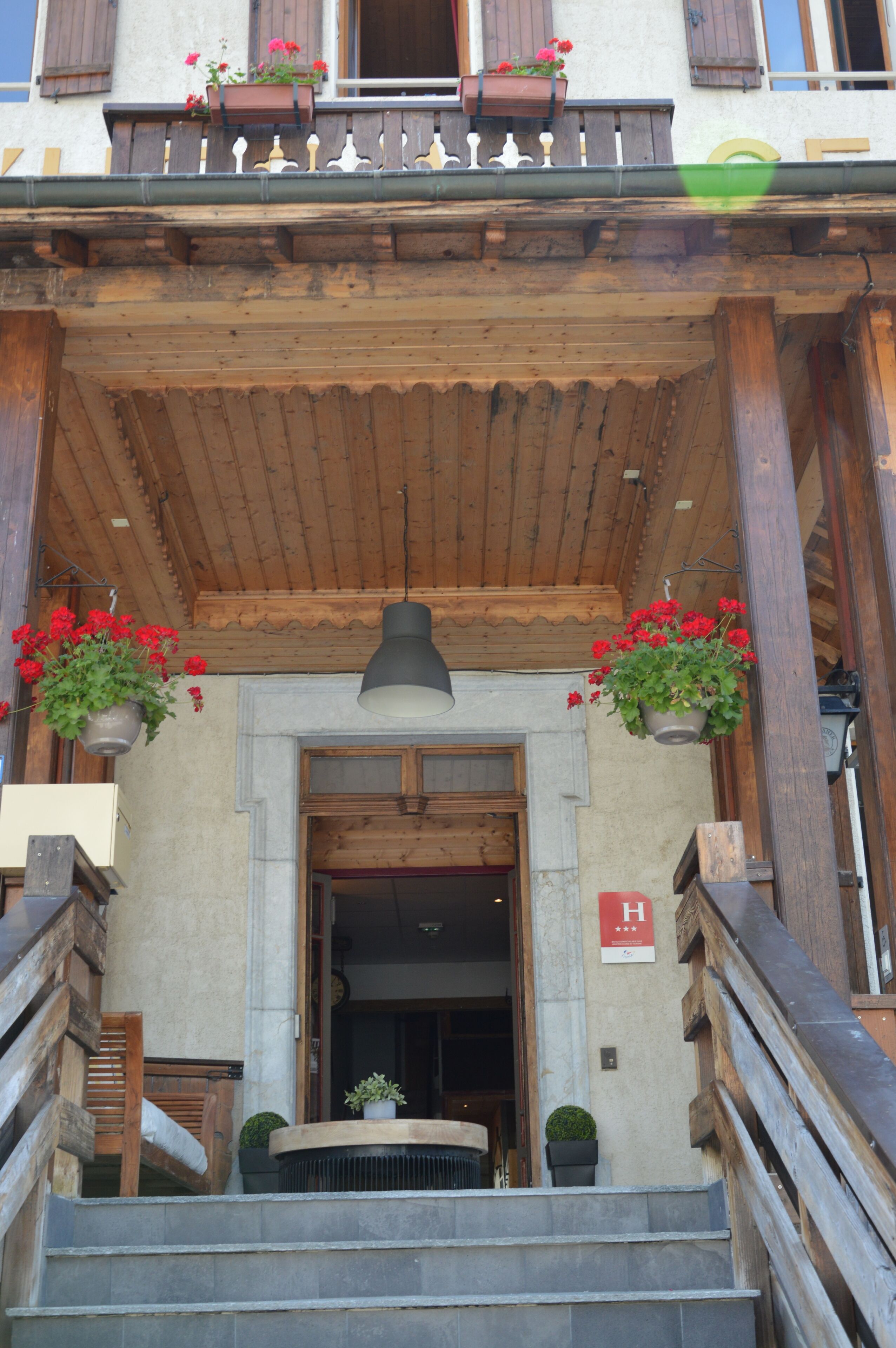 Una escalera de madera que lleva a la entrada de un edificio, con un colgador de luces y plantas en macetas.