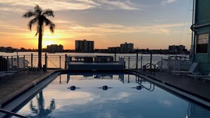 Ein Swimmingpool mit Sonnenuntergangsblick, eine Palme und eine Stadtlandschaft im Hintergrund.