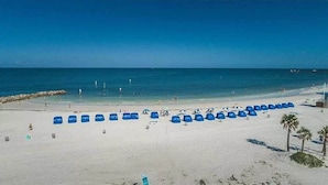 Ein Strand mit Reihen blauer Liegen und Sonnenschirmen, einem sandigen Ufer und einem klaren, blauen Himmel.