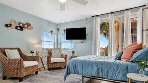 Ein Schlafzimmer mit einem Bett, zwei Korbstühlen, einem kleinen Tisch, einem Fernseher und einem Fenster mit Vorhängen.