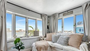 A cozy room with a sofa, a potted plant, and a view of the city. - Right on Clearwater Beach! Corner Suite Waterview (Clearwater)
