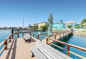 Waterfront boardwalk with boat slips and seating leads to colorful coastal buildings, offering direct water access and tropical island living. - Boho Studio B-4: Intracoastal Views, Shared Heated Pool & Dock (Clearwater)