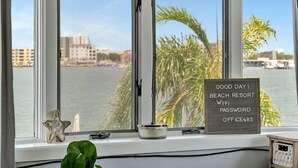 A window with a view of a body of water, palm trees, and buildings. - Right on Clearwater Beach! Corner Suite Waterview (Clearwater)