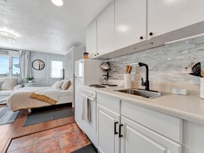 A compact, modern kitchen with white cabinetry, a stainless steel sink, and a tiled backsplash. - Right on Clearwater Beach! Corner Suite Waterview (Clearwater)