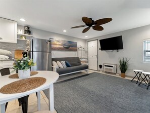Ein modernes Wohnzimmer mit einer Couch, einem Esstisch mit Platzsets, einem Deckenventilator, einem Flachbildfernseher und einem Gemälde an der Wand.