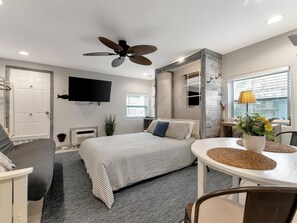A modern bedroom with a bed, a desk, a chair, a ceiling fan, a TV, and a window with blinds. - Walk 2 minutes to the Beach! Enjoy the Heated Pool (Clearwater)