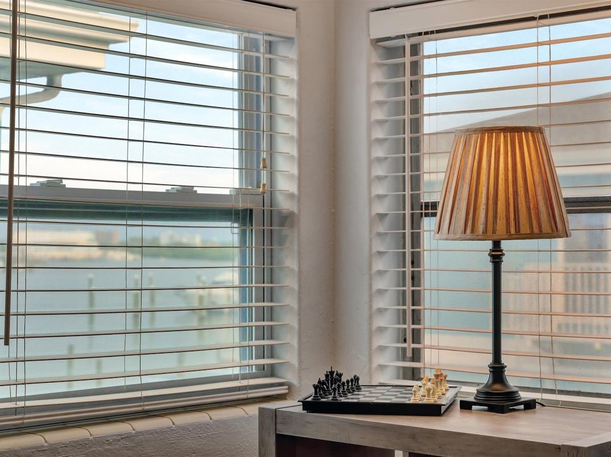 A room with a chessboard and a lamp near a window with blinds.