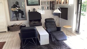 A modern living room with a fireplace, a black leather sofa, a white side table, and a large poster of a jazz musician. - 8 Person Holiday Home in Maribo (Maribo)