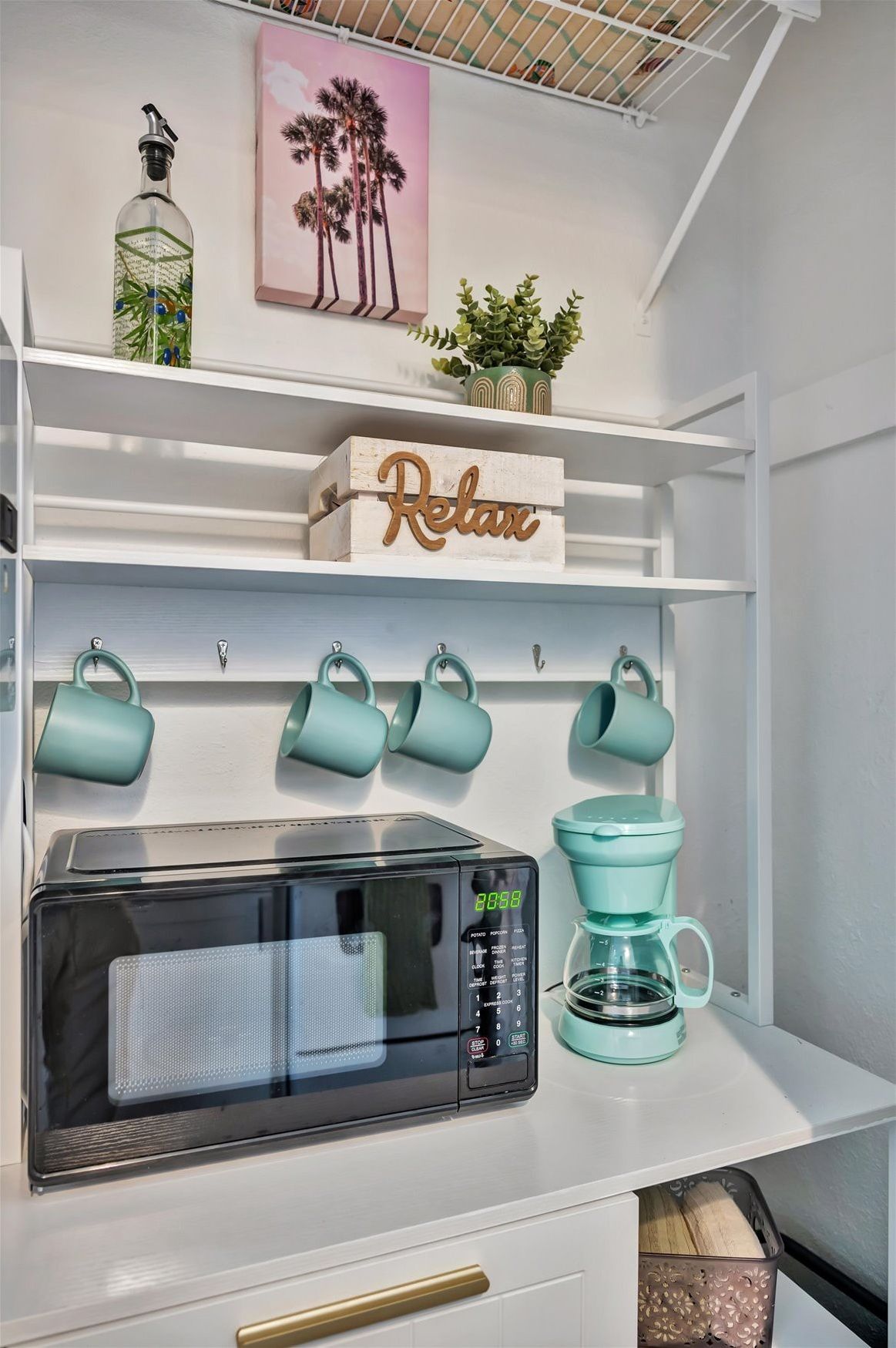Une cuisine équipée d’un four à micro-ondes, d’une machine à café, de tasses de couleur turquoise et d’une pancarte « Détendez-vous » posée sur une étagère.