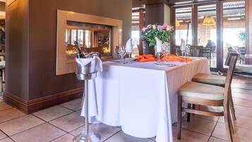 A dining area with a table set for two, a fireplace, and a view of the outdoors.