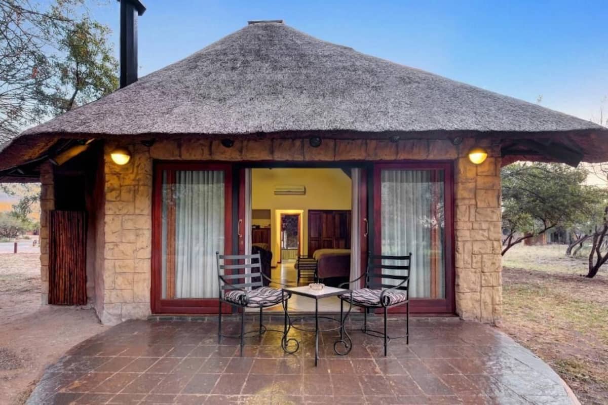 Una estructura con techo de paja y un patio con dos sillas y una mesa.