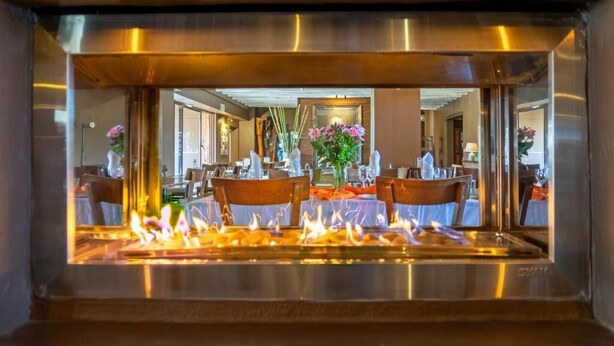 Un restaurant doté d’un foyer central, de tables avec des chaises et de fleurs décoratives.