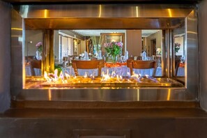 A restaurant with a central fire feature, tables with chairs, and decorative flowers. - Zebula Golf Estate & Spa (Bela Bela)