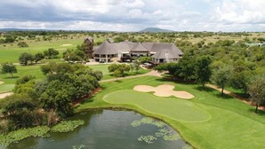Un parcours de golf avec un étang, entouré d’arbres et bordé d’un grand bâtiment comprenant plusieurs structures.