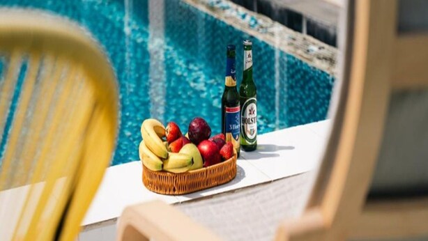 A poolside area with a wicker basket of fruit and two bottles of beer on a white surface. - Sunday Gateway Jeddah Formerly Beach Garden Hotel (Jeddah)