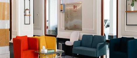 A modern lobby with a seating area featuring a glass coffee table, a red armchair, a yellow armchair, and a teal sofa.