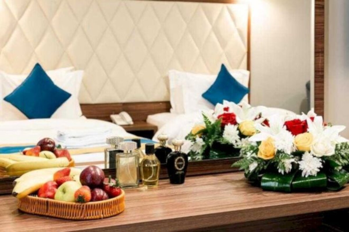 A hotel room with a bed, a bedside table with fruits, flowers, and toiletries.