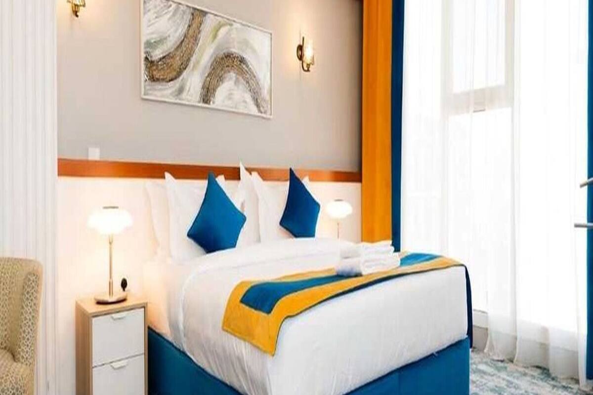 A hotel room with a bed, bedside tables, a lamp, a painting, and a window with curtains.