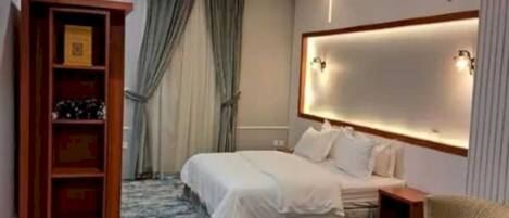 A hotel room with a bed, a bedside table, a chair, a bookshelf, and a large window with curtains.