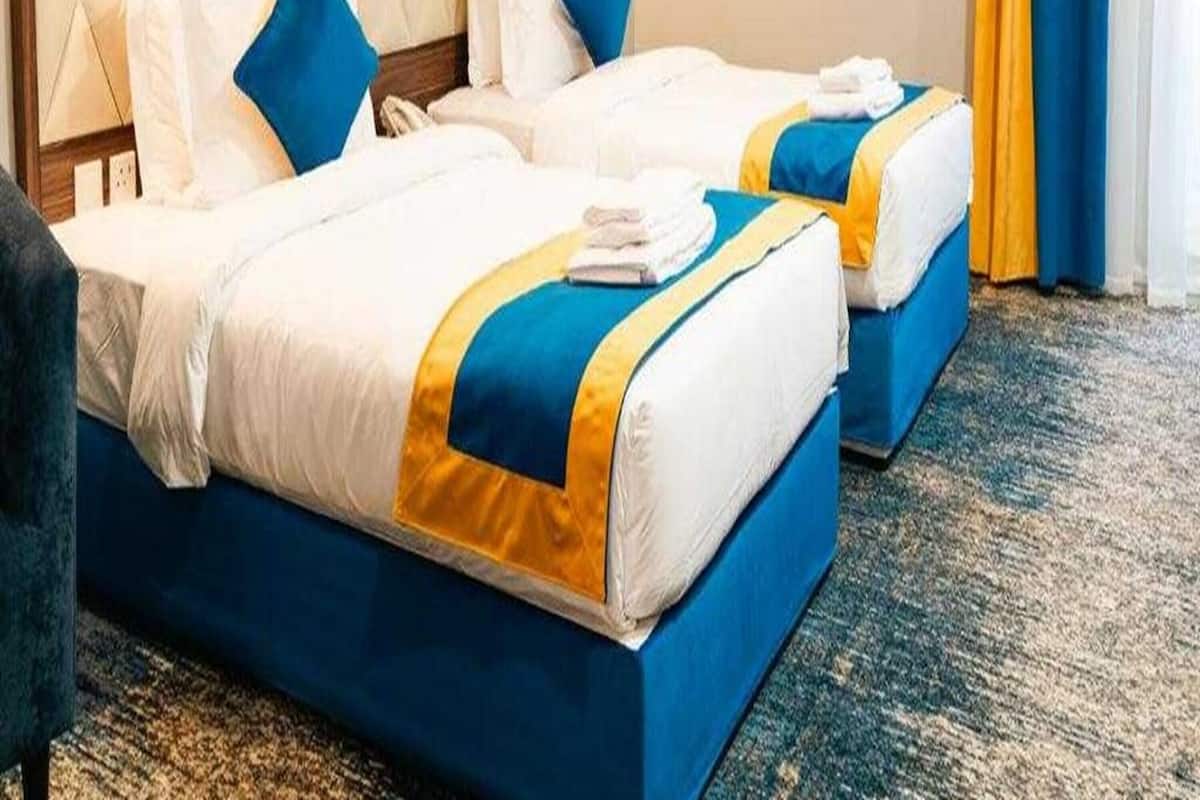 A hotel room with two beds, each with blue and white bedding and a yellow accent.