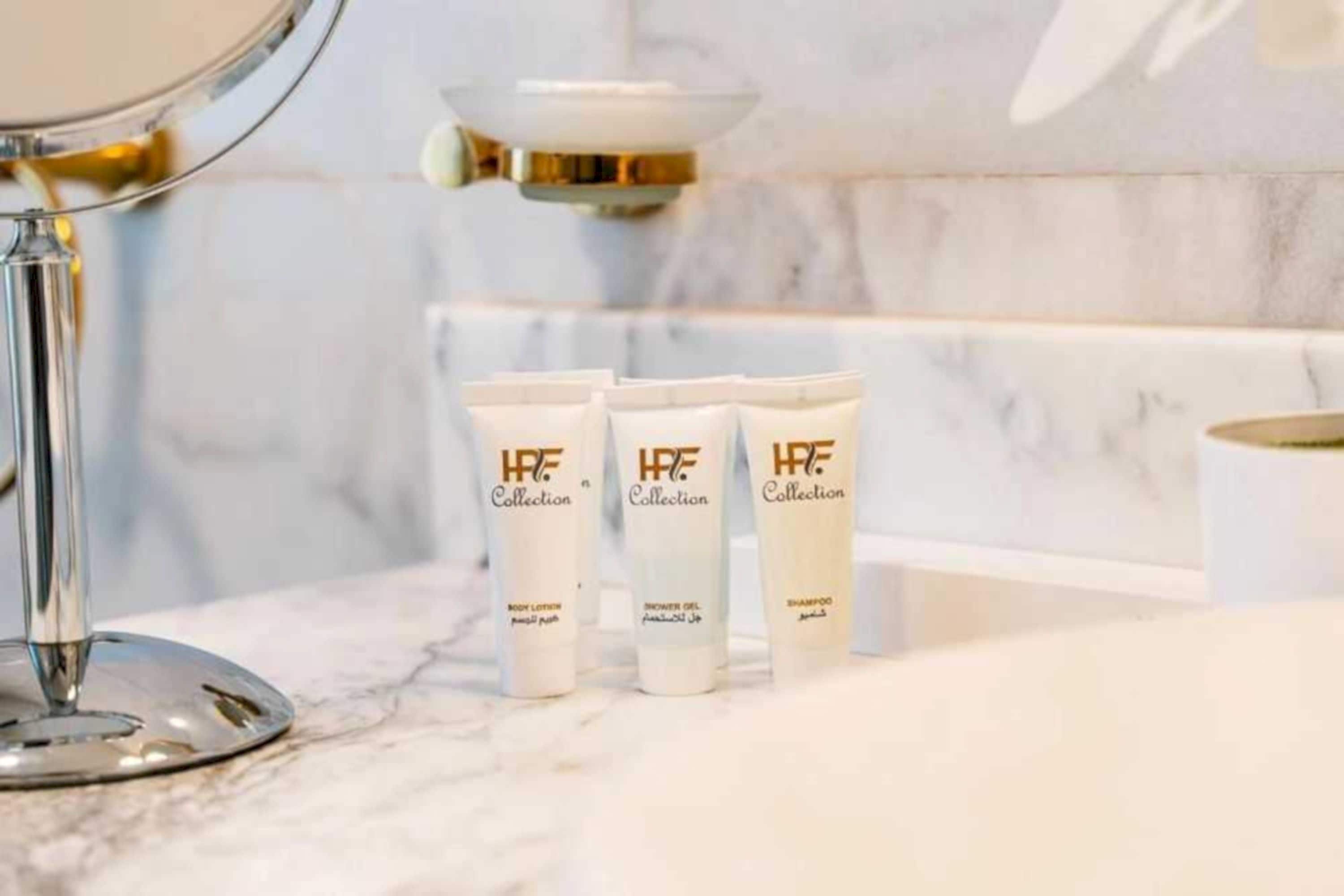 A bathroom with a marble countertop, a mirror, and three tubes of H&F Collection body lotion.