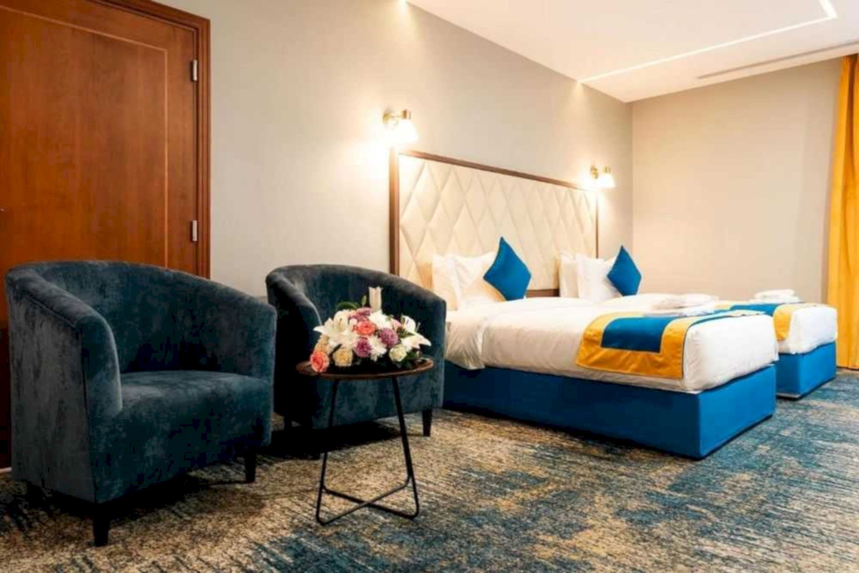 A hotel room with a bed, two armchairs, a small table with a floral arrangement, and a carpeted floor.