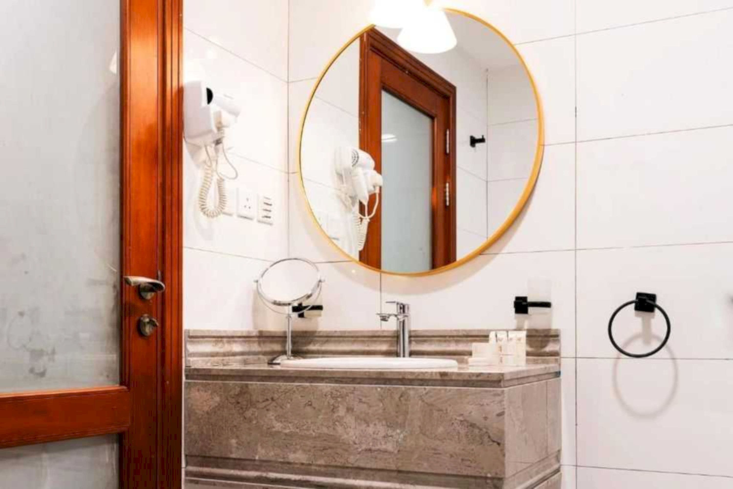 Un bagno con lavabo in marmo, uno specchio rotondo, un asciugacapelli e un porta asciugamani.
