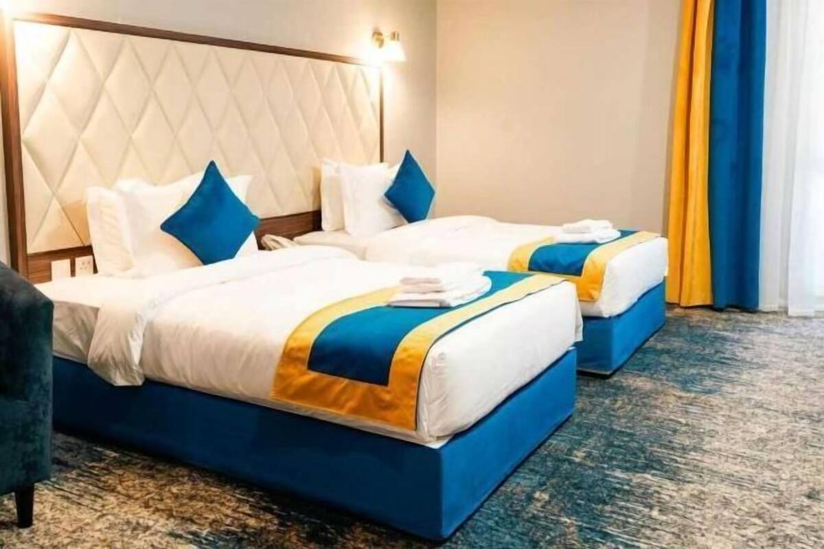 A hotel room with two beds, a headboard, a carpeted floor, and a curtain.