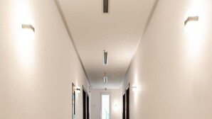 A long, narrow hallway with white walls and a wooden floor. There are two light fixtures on the walls and a ceiling vent. - Sunday Gateway Jeddah Formerly Beach Garden Hotel (Jeddah)