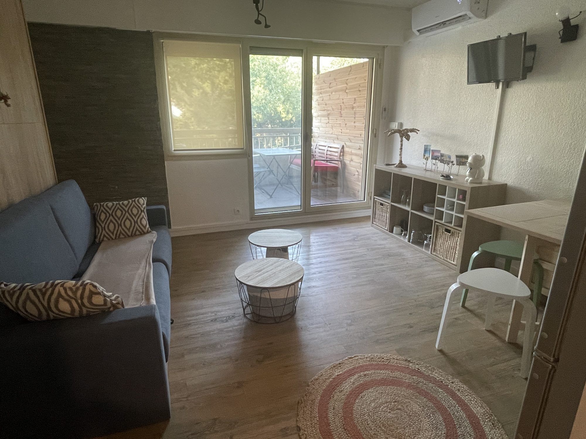 A living room with a sofa, two small tables, a rug, and a sliding glass door leading to an outdoor area.